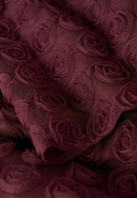 Burgundowy teksturowany materiał z wzorem wypukłych kształtów róż, wykonany z przezroczystego, lekkiego materiału, z delikatnym i szczegółowym wzorem.