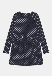 Långärmad klänning i marinblått med vita prickar, med en samlad kjol och rund halsringning. Tillverkad i ett mjukt, slätt tyg.