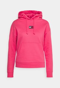 Felpa rosa brillante con tasca frontale e patch con logo "Tommy Jeans" centrato sotto il cappuccio regolabile.