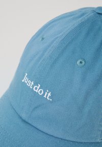 Sininen puuvillainen baseball-lakki, jossa on teksturoitu kangas, kaareva lippa ja valkoisella brodeerattu teksti "Just do it." etupaneelissa.