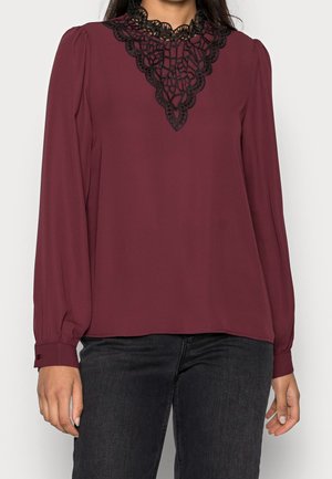 Blusa bordeaux con maniche lunghe, caratterizzata da un elegante scollo in pizzo nero. Tessuto morbido con vestibilità comoda e polsini con bottoni.