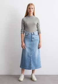 Lichtgrijze geribde lange mouwen top met een gefronste halslijn, gecombineerd met een high-waisted lichtblauwe denim maxi rok en witte sneakers.