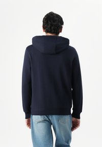 Hoodie bleu marine avec capuche à cordon, coupe régulière, manches longues et poignets côtelés. Texture douce, design minimaliste et sans logos visibles.