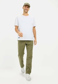 Hvid kortærmet t-shirt, olivengrønne bukser, hvide sneakers; afslappet pasform med en rektangulær form, glat tekstur og minimal branding.