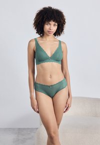 Conjunto de lingerie verde com um bralette adornado com renda e cuecas combinando que apresentam uma textura subtil e um pequeno detalhe decorativo na parte da frente.