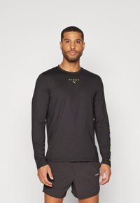 Schwarzes Langarm-Athletikshirt mit gelbem "HYROX"-Logo auf der Brust und Druck auf dem linken Arm, gefertigt aus leichtem, feuchtigkeitsableitendem Material.