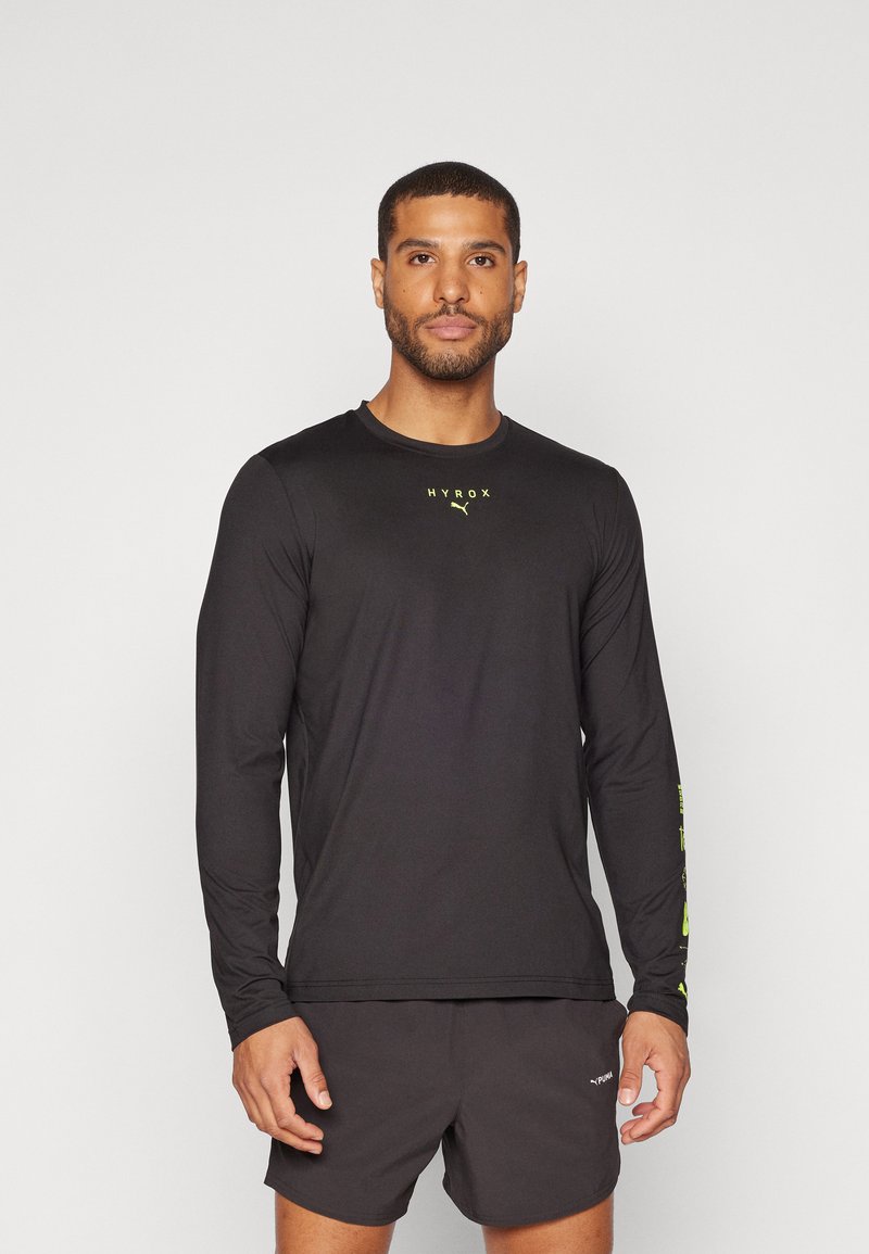 Schwarzes Langarm-Athletikshirt mit gelbem "HYROX"-Logo auf der Brust und Druck auf dem linken Arm, gefertigt aus leichtem, feuchtigkeitsableitendem Material.