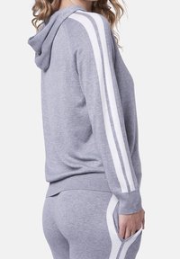 Sudadera gris con tejido texturizado, que presenta rayas blancas a lo largo de las mangas y un bolsillo tipo canguro. Diseñada con un ajuste relajado y capucha.