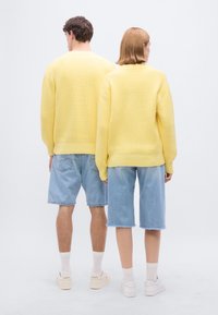 Κίτρινες πουλόβερ με υφή συνδυασμένα με ανοιχτόχρωμα μπλε τζιν σορτς. Και οι δύο εμφανίσεις περιλαμβάνουν λευκά αθλητικά παπούτσια και ορατά καλτσάκια που φαίνονται πάνω από τους αστραγάλους.