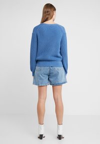 Blå ribbad stickad tröja med rund halsringning, ihop med ljusa denimshorts. Modellen bär vita ankelstövlar med klumpig klack.