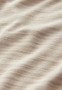 Tela suave de color beis con una textura fina y acanalada, y sutiles variaciones en el tono, creando una apariencia ondulada. Ideal para ropa o tapicería.