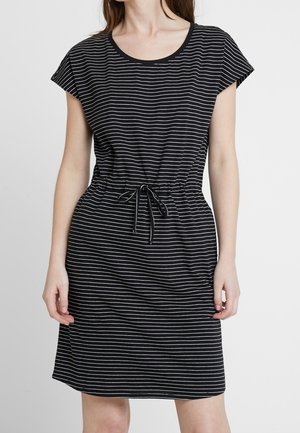 Woman wearing a black, short-sleeve dress with white horizontal stripes and a drawstring waist, standing against a plain light background.