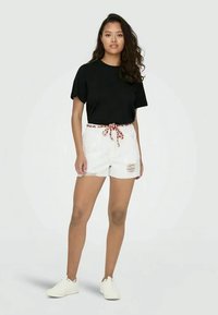 Svart t-skjorte med korte ermer kombinert med hvite denimshorts med et mønstret snor og slitte detaljer. Hvite sneakers fullfører antrekket.