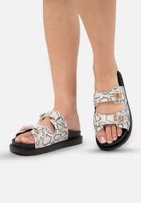 Sandales à imprimé serpent noir et blanc avec deux boucles réglables, semelle noire plate et brides texturées. Design ouvert à l'avant.