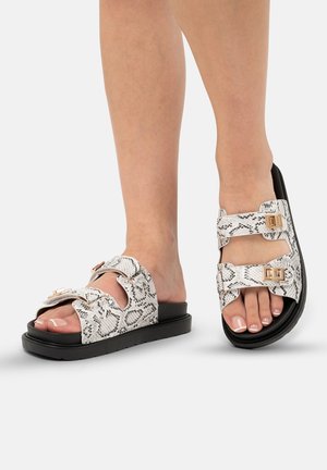 Sandali con stampa serpente bianca e nera, dotati di due fibbie regolabili, suola nera piatta e cinturini texturizzati. Design open-toe.