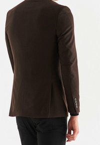 Blazer marrone su misura con un design elegante, tessuto testurizzato e spacchetto singolo. Presenta quattro bottoni sui polsini e una silhouette aderente.