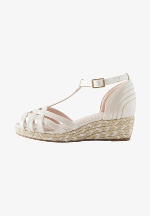 White wedge sandal featuring a woven jute sole, crisscross strappy design, and an adjustable ankle strap with a gold buckle detail.