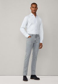 Light blue button-up shirt, gray slim-fit jeans, and dark blue suede shoes. Simple design with long sleeves and classic collar.
