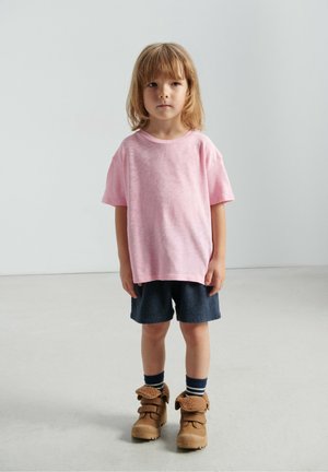 Pink cotton t-shirt with short sleeves, paired with navy textured shorts and brown boots featuring a fuzzy fur-like accent.