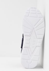 Skofot med en texturerad vit gummisula som visar ett geometriskt mönster; mörk marinblå överdel synlig vid skoens kant.