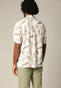 Korte mouwen shirt van lichtgewicht stof, met een witte achtergrond en tropische bladeren en bloemenpatronen in beige en roze tinten.