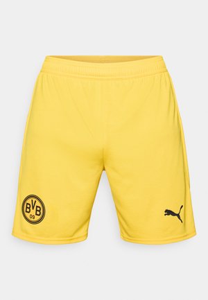 Shorts de sport jaunes en tissu léger avec une taille élastique. Présente un logo circulaire noir sur la jambe gauche et un logo Puma noir.
