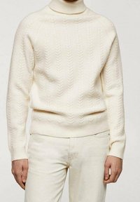 Strickpullover mit Rollkragen in Creme, aus weicher Wolle, mit geripptem Saum und Bündchen, kombiniert mit hellen Jeans.