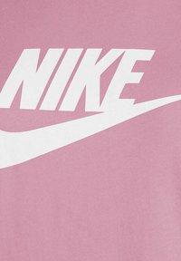 T-shirt in cotone rosa con grande logo bianco "NIKE" e grafica dello swoosh, che mette in evidenza una texture liscia e una tipografia audace.