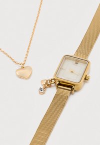 Ρολόι με χρυστό πλέγμα και τετράγωνο καντράν, λευκό καντράν και τρεις δείκτες· συνοδευόμενο από χρυσή αλυσίδα με μενταγιόν καρδιάς.