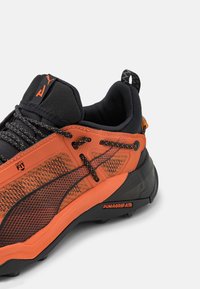 Baskets de sport orange et noir avec une tige en maille texturée, une semelle extérieure en caoutchouc, un design multiforme et un talon renforcé ainsi qu'un système de laçage.