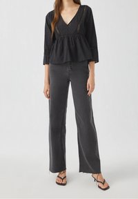 Top peplum nero con punti testurizzati e scollatura a V, abbinato a jeans grigi a vita alta e gamba dritta e sandali neri con cinturini.