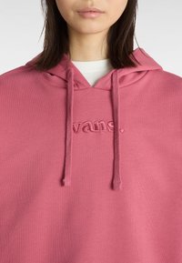 Rosa hoodie med dragsko i huvan, med en broderad "vans." logotyp på framsidan. Tillverkad av mjukt, texturerat material.