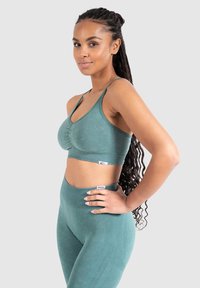 Sostén deportivo verde con un diseño de escote en V y frente fruncido, combinado con leggings de cintura alta que presentan una textura suave y patrones sutiles.