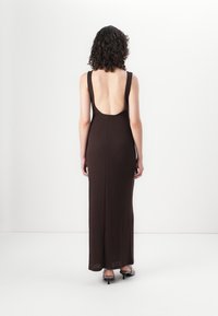 Vue arrière d'une longue robe en tricot côtelé marron sans manches avec une découpe profonde dans le dos, présentant une silhouette ajustée et une texture subtile.