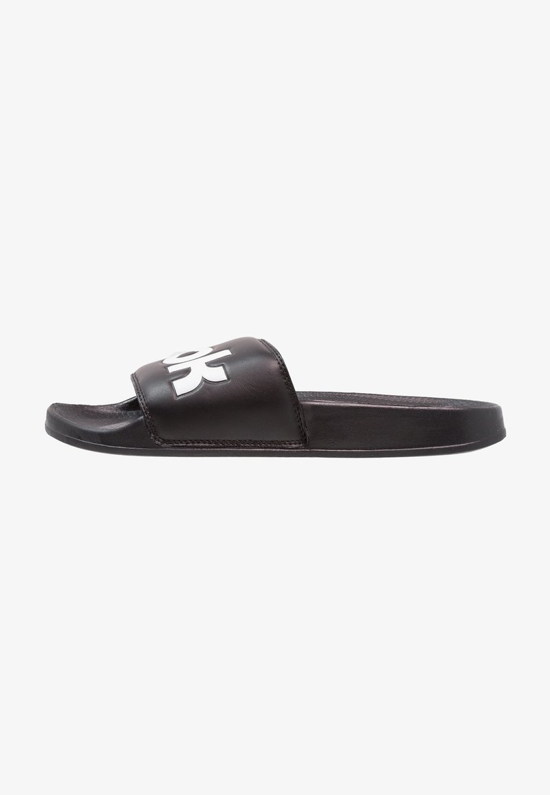 Sandale slide noire avec une large sangle comportant un logo blanc stylisé, semelle plate et design à bout ouvert, isolée sur fond blanc.
