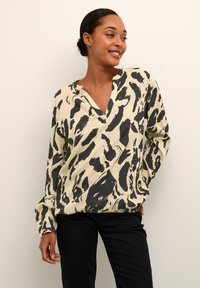 Blusa de manga larga color crema con estampado abstracto en negro, con escote en V y un corte holgado, fabricada en una tela suave y ligera.