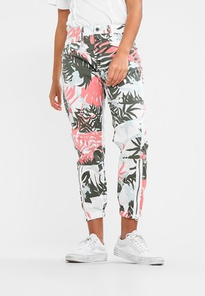 Patroon joggingbroek met een ontwerp van groene, roze en witte tropische bladeren. Bevat elastische boorden en ritsaccenten. Draagt bij witte sneakers.