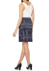 Falda de patrón navy con diseños geométricos y florales, presenta una textura suave y un corte recto. Combinada con zapatos de tacón altos navy.