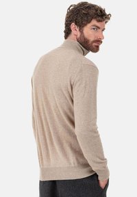 Beiger Kaschmir-Rollkragenpullover mit langen Ärmeln, mit geripptem Saum und weicher Textur, Rückansicht.