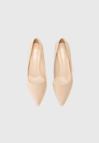 Un par de bailarinas beige de punta con acabado de ante y la marca "RAID" impresa en el interior de cada zapato, exhibidas sobre un fondo blanco.