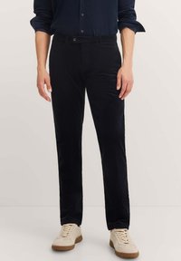 Black corduroy trousers with a straight-leg design, featuring a button closure and front pockets. Worn with light-colored sneakers.