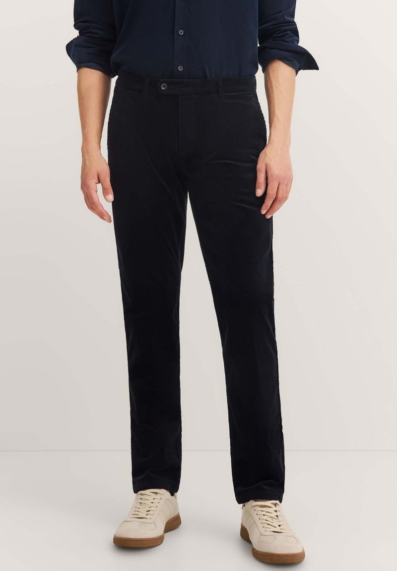 Black corduroy trousers with a straight-leg design, featuring a button closure and front pockets. Worn with light-colored sneakers.