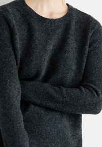 Suéter de lã cinza escuro com decote redondo e mangas longas. O tecido de malha texturizado apresenta pequenas manchas sutis. Design clássico e ajustado.