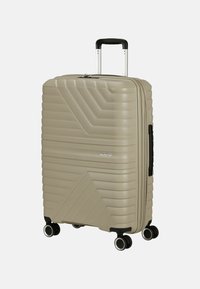 Valigia rigida beige con motivo a zigzag testurizzato. Dotata di manico telescopico, quattro ruote e chiusura a zip.