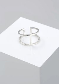 Anillo de plata con diseño abierto y geométrico que presenta elementos circulares y lineales. Superficie lisa y reflectante sobre un fondo blanco.