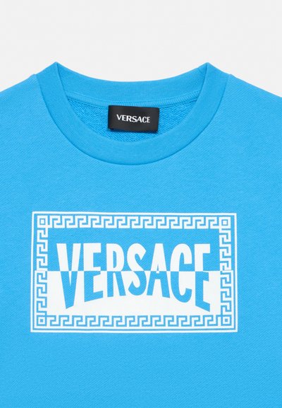 Chemise bleu vif avec un logo Versace blanc à l'intérieur d'un rectangle à motif clé grecque sous le col.