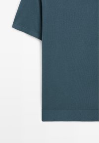 Ciemnozielona bawełniana koszulka z krótkim rękawem, z okrągłym dekoltem i prostym wykończeniem dołu. Miękka struktura i minimalistyczny design.