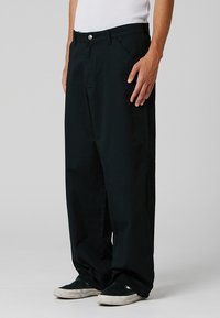 Pantalon noir ample en coton, doté d'une fermeture à boutons et de poches avant. Texture lisse avec une silhouette à jambes droites.