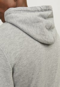 Gray hoodie with a soft, textured fabric. Features a rounded hood and visible stitching along the edges. Simple, unembellished design.