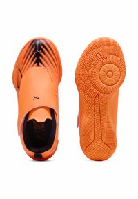 Kirkkaat oranssit Puma-urheilukengät mustilla yksityiskohdilla, joista toinen näyttää päällysnäkymän Velcro-hihnalla ja toinen teksturoitu pohja, jossa on Puma-logo.